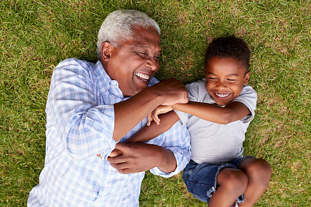A grandfather and his young grandson lying on the grass, laughing together